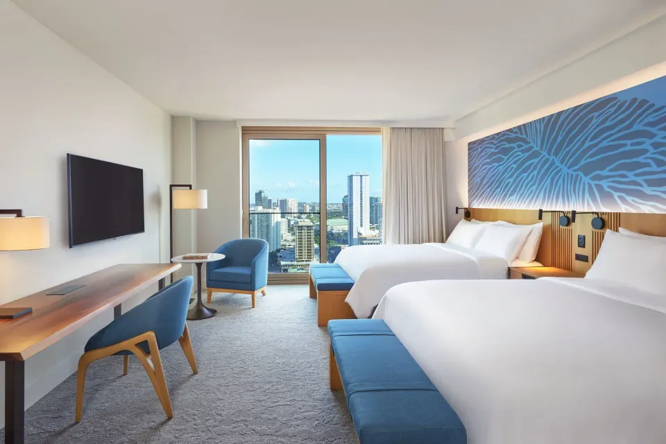 Two-bed City View room at Renaissance Honolulu Hotel & Spa with desk, TV, blue chair, and city window.