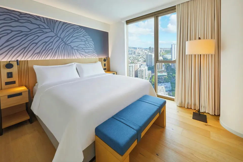 King bed in an Ocean View one-bedroom suite at Renaissance Honolulu Hotel & Spa beside a tall city window.