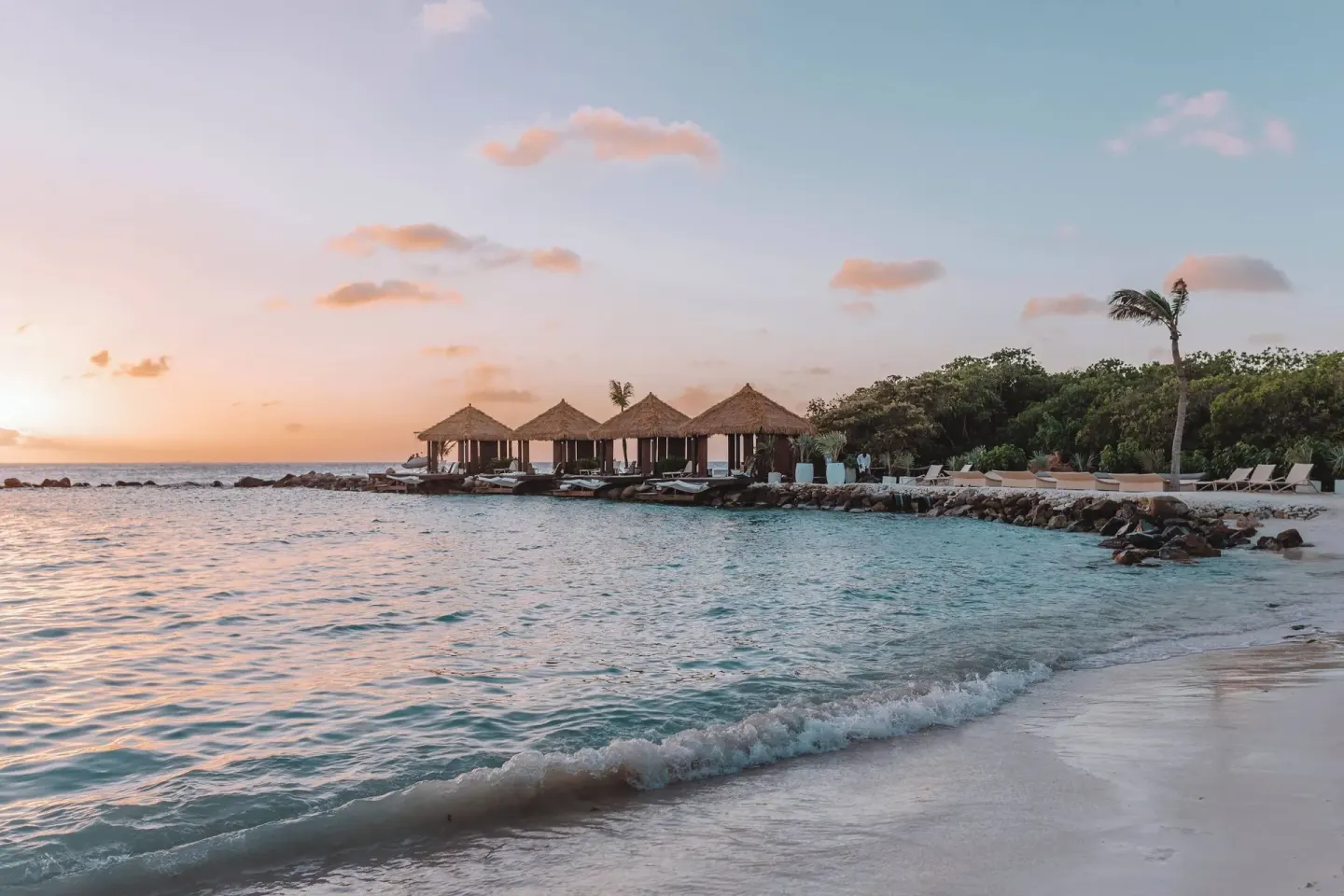 A sandy beach with cabanas and calm surf at Renaissance Wind Creek Aruba Resort.