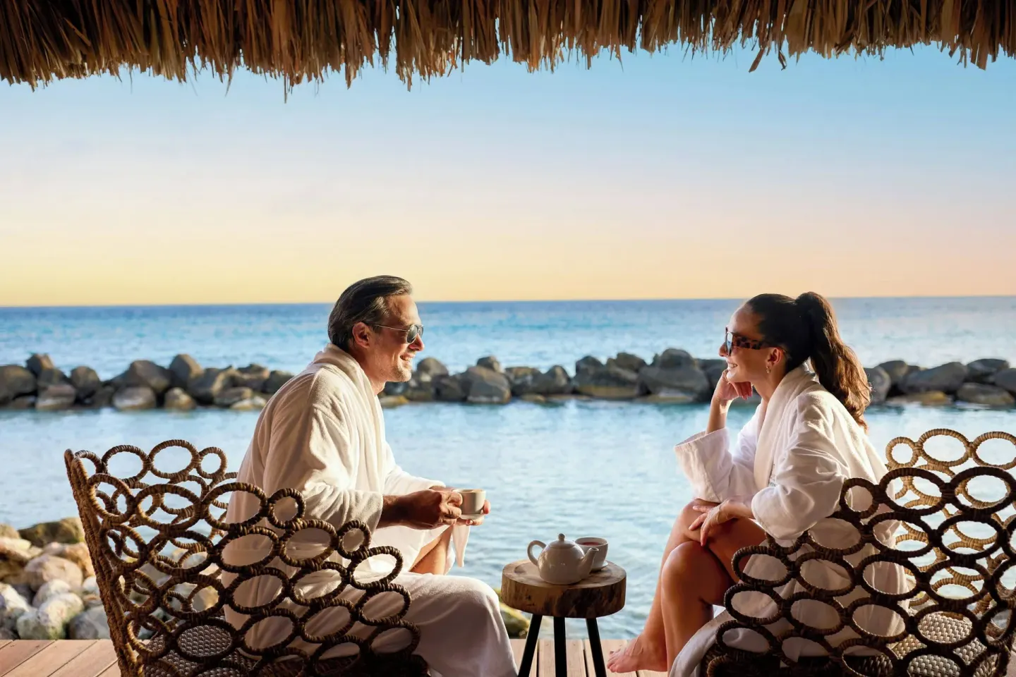 Guests in robes seated by the ocean at Renaissance Wind Creek Aruba Resort.