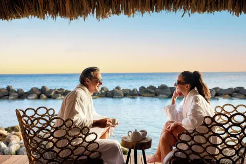 Guests in robes seated by the ocean at Renaissance Wind Creek Aruba Resort.