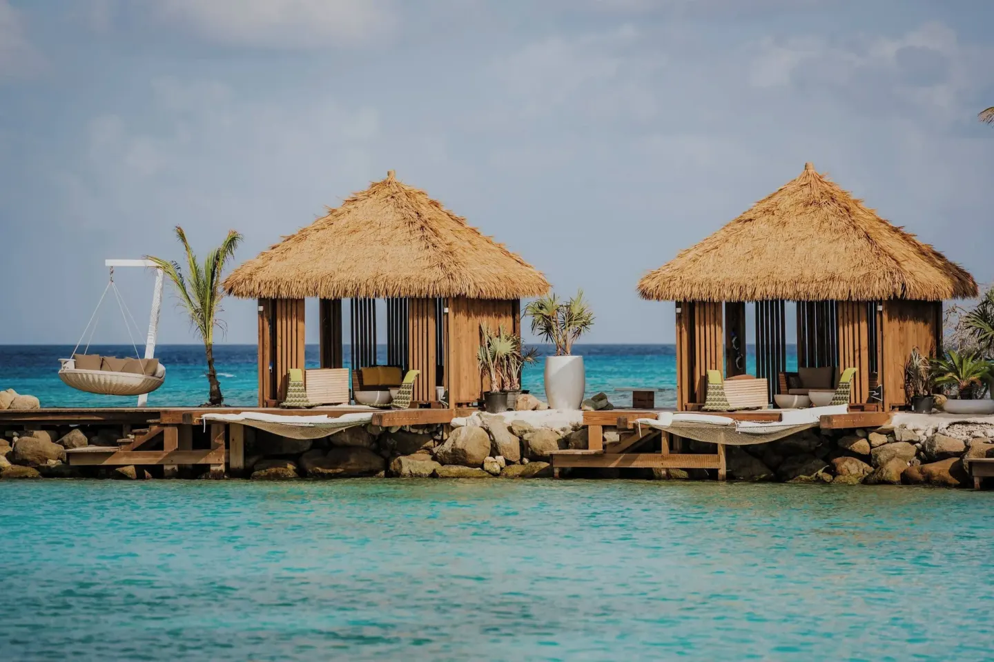 Thatched overwater cabanas stand beside turquoise water at Renaissance Wind Creek Aruba Resort.