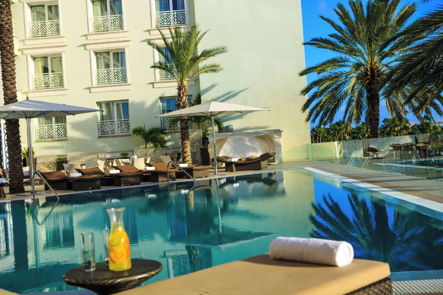 Pool with lounge chairs, umbrellas and palms at Renaissance Wind Creek Aruba Resort.