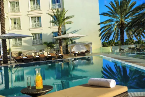 Pool with lounge chairs, umbrellas and palms at Renaissance Wind Creek Aruba Resort.