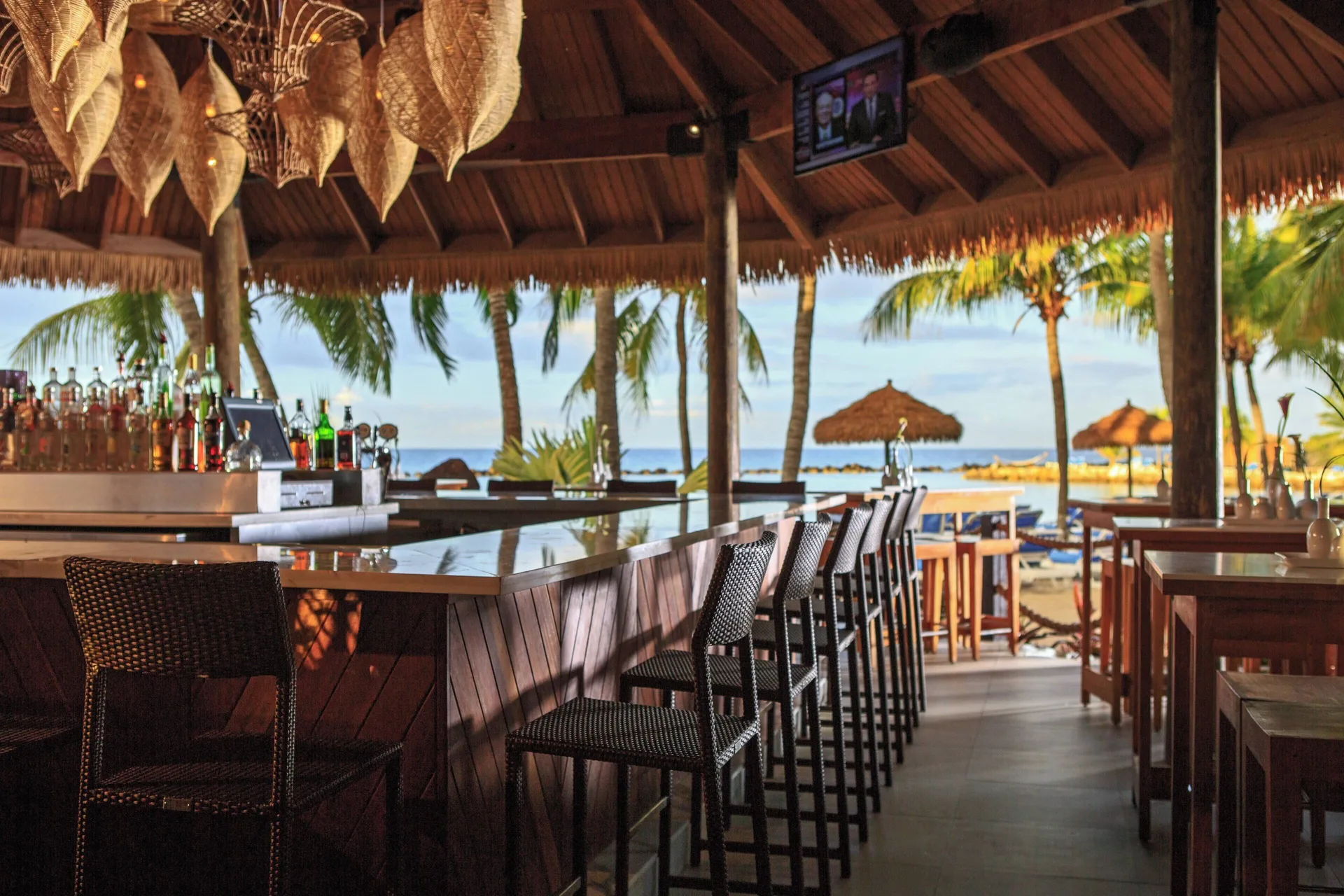 Open-air beach bar with stools and ocean view at Renaissance Wind Creek Aruba Resort.