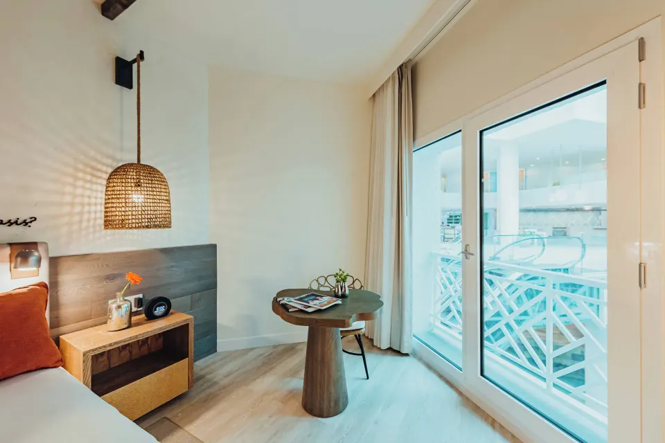 Guest room with bed, table, balcony doors, and poolside view at Renaissance Wind Creek Aruba Resort.