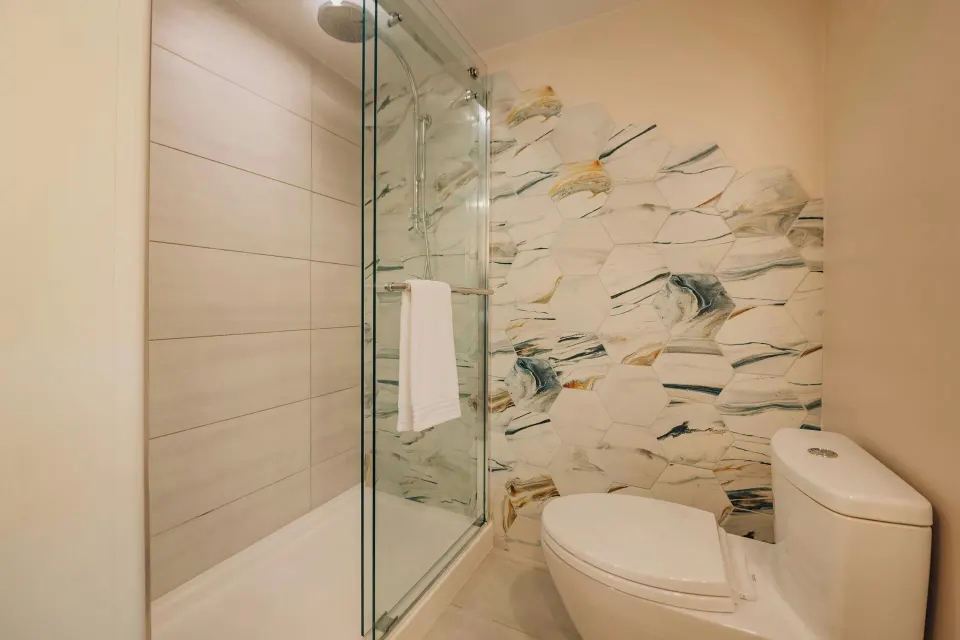 Suite bathroom with glass shower, toilet, and patterned tile at Renaissance Wind Creek Aruba Resort.