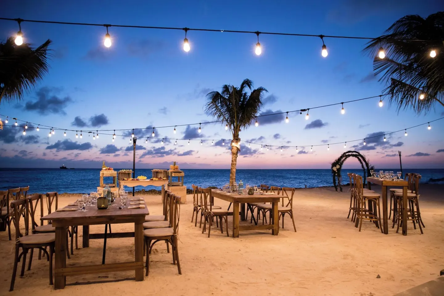 Beach dinner tables under string lights at Renaissance Wind Creek Aruba Resort.