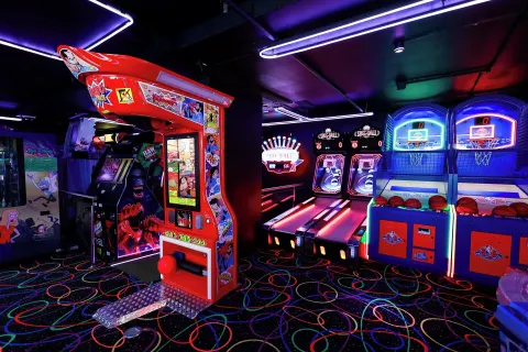 Arcade basketball and game machines glow under neon lights at Renaissance Wind Creek Curacao Resort.