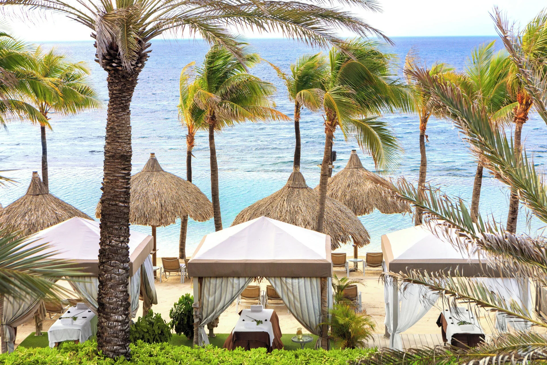 Beach cabanas and palm trees by the water at Renaissance Wind Creek Curacao Resort.