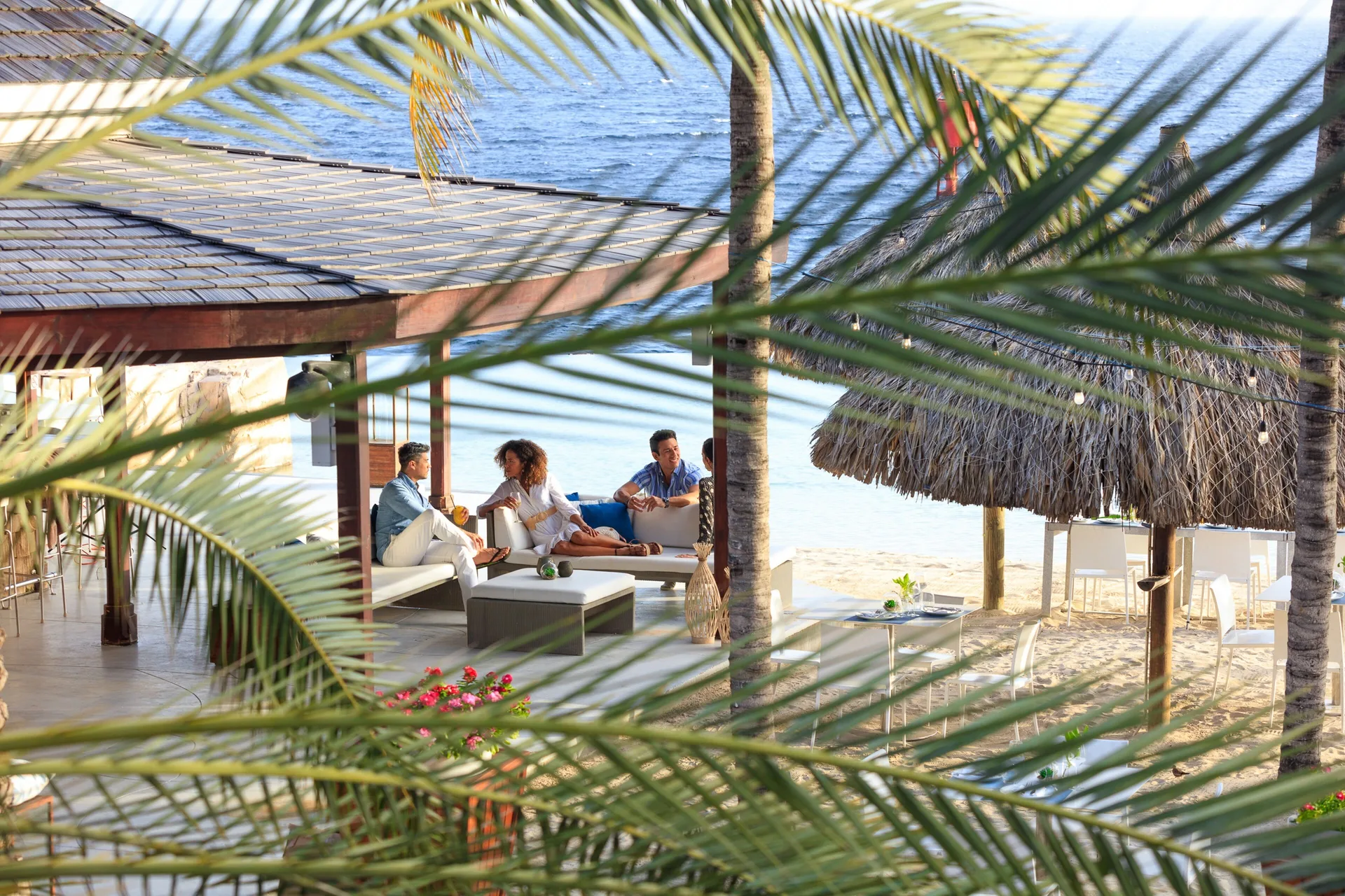 Beachside lounge seating viewed through palm fronds at Renaissance Wind Creek Curacao Resort.