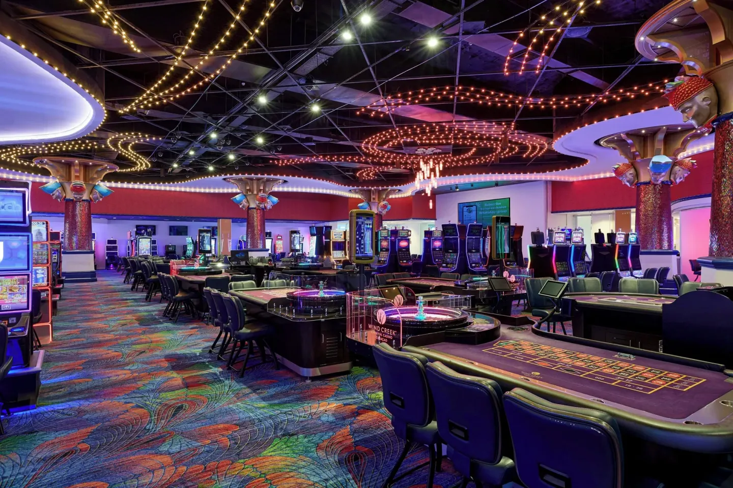 Casino tables and slot machines under colorful ceiling lights at Renaissance Wind Creek Curacao Resort.