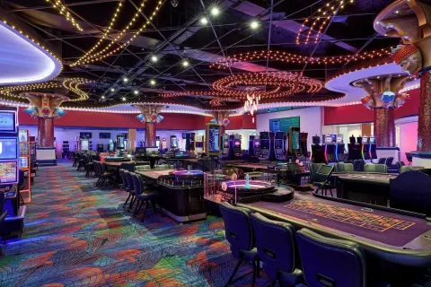 Casino tables and slot machines under colorful ceiling lights at Renaissance Wind Creek Curacao Resort.