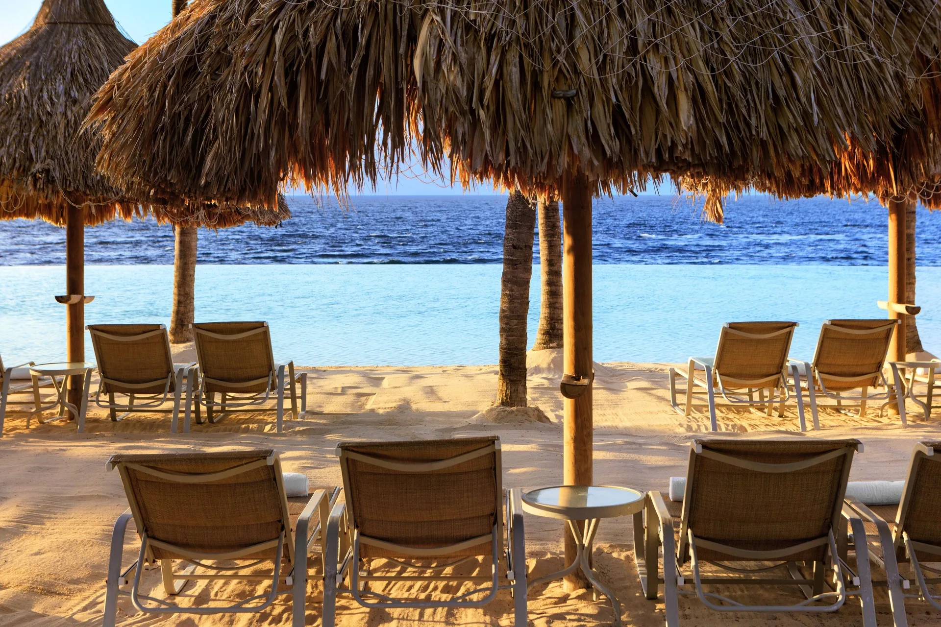 Lounge chairs sit under thatched shade by the water at Renaissance Wind Creek Curacao Resort.