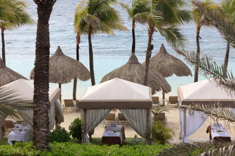 Spa cabanas among palms on the beach at Renaissance Wind Creek Curacao Resort.