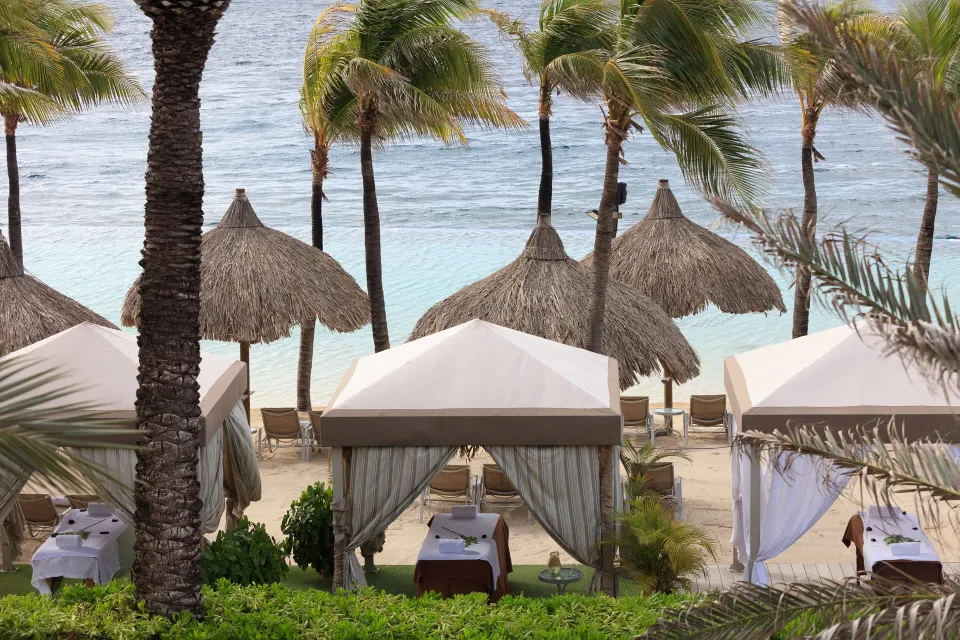 Spa cabanas among palms on the beach at Renaissance Wind Creek Curacao Resort.