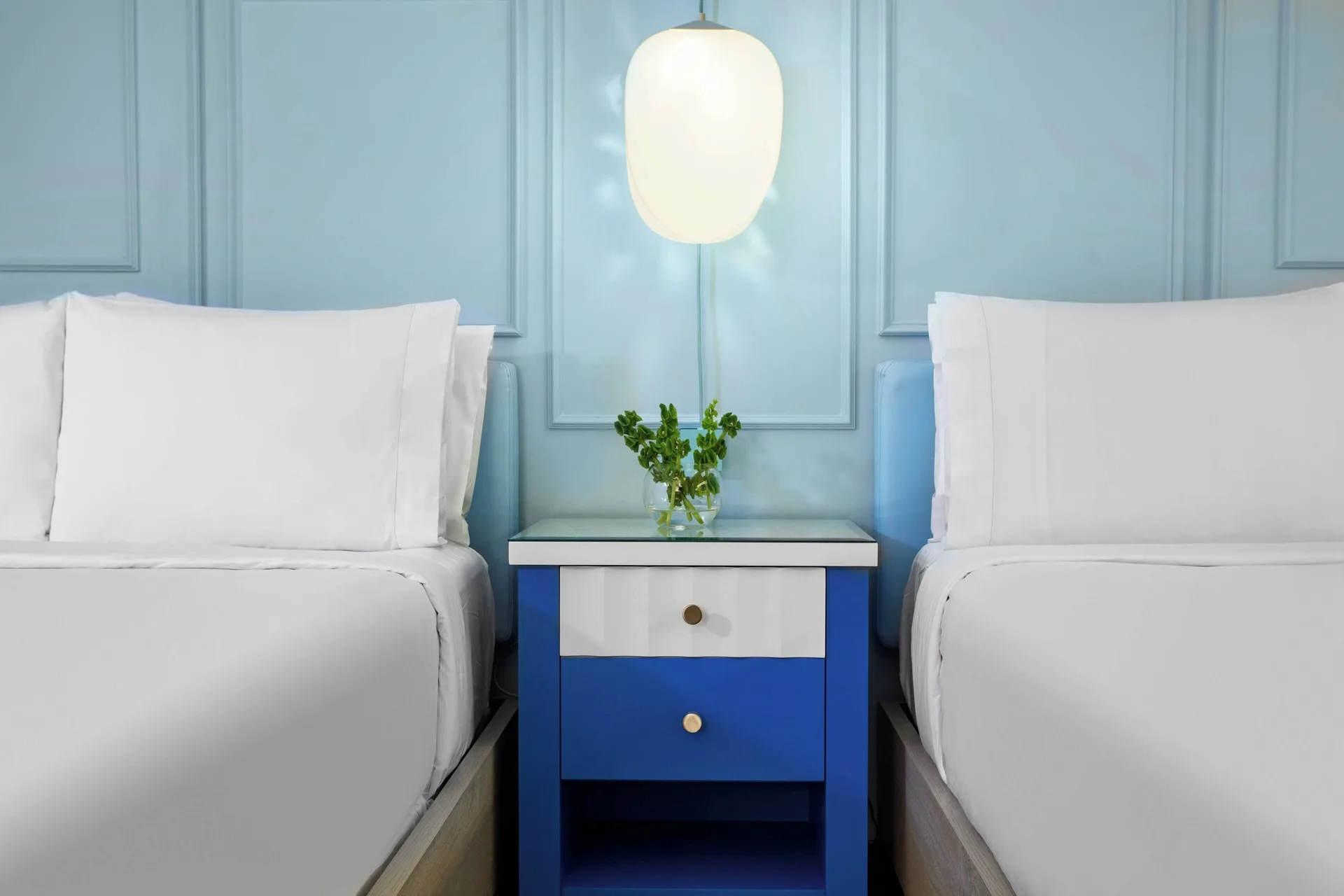 Two white beds with a blue nightstand at Renaissance Wind Creek Curacao Resort.