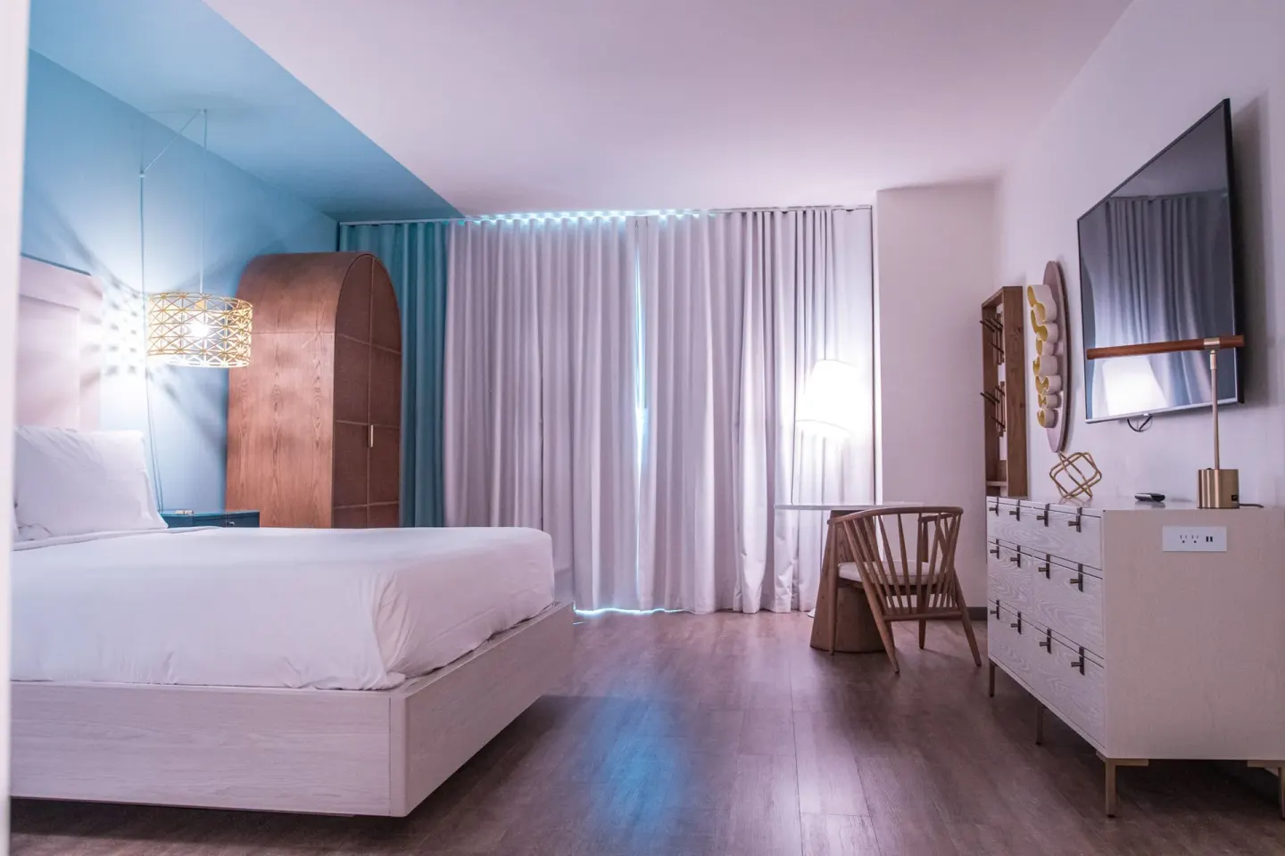 One bedroom suite king bed with dresser, desk and curtains at Renaissance Wind Creek Curacao Resort.