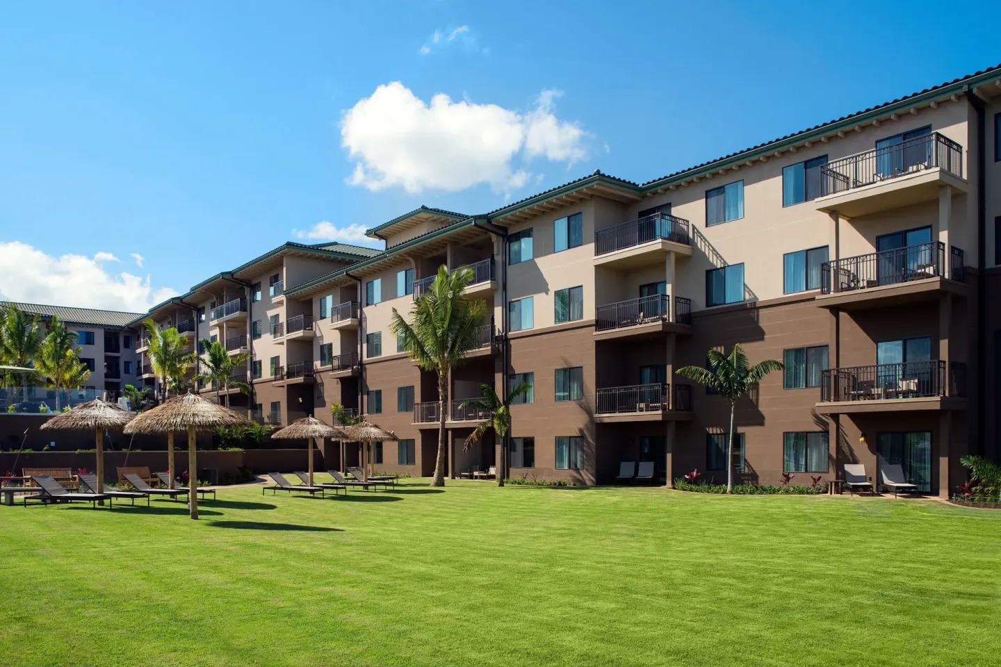 Guestroom building, lawn, palms and thatched shade umbrellas at Residence Inn Maui Wailea.