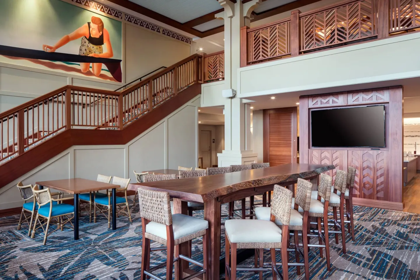 Communal lobby table, staircase, and wall mural at Residence Inn Maui Wailea.
