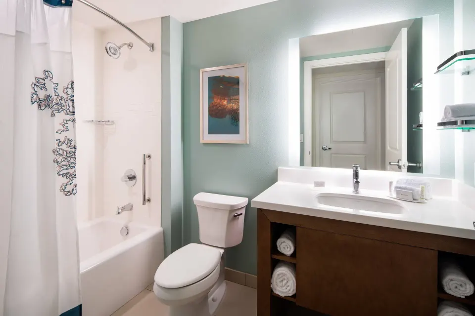 Suite bathroom at Residence Inn Maui Wailea with tub shower, toilet, vanity, mirror, and open shelving.