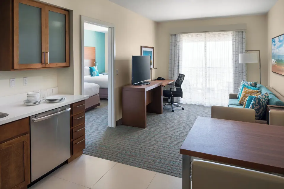 Suite kitchen and living area at Residence Inn Maui Wailea with dishwasher, dining table, sofa, desk, and balcony doors.