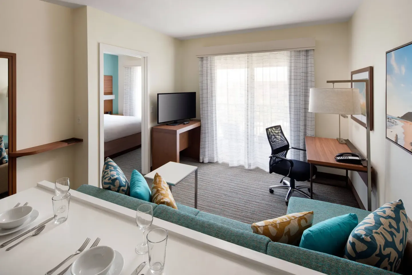 One-bedroom suite living area at Residence Inn Maui Wailea with sofa, desk, dining counter, and balcony doors.
