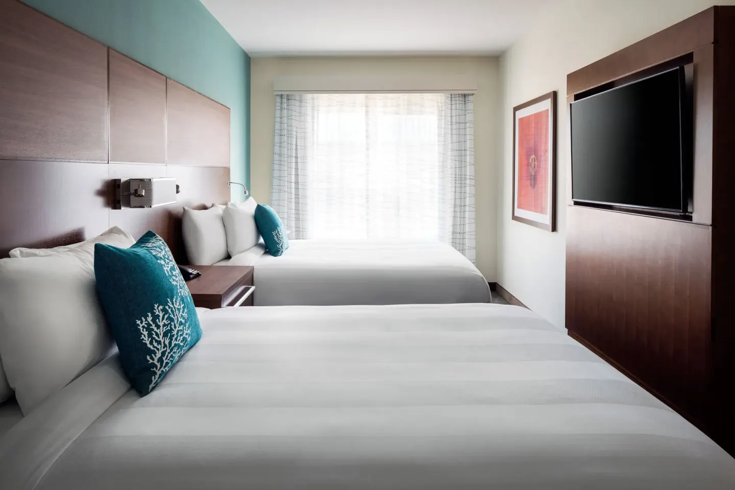 Two-bed suite bedroom at Residence Inn Maui Wailea with teal pillows, wood headboard, and TV wall.