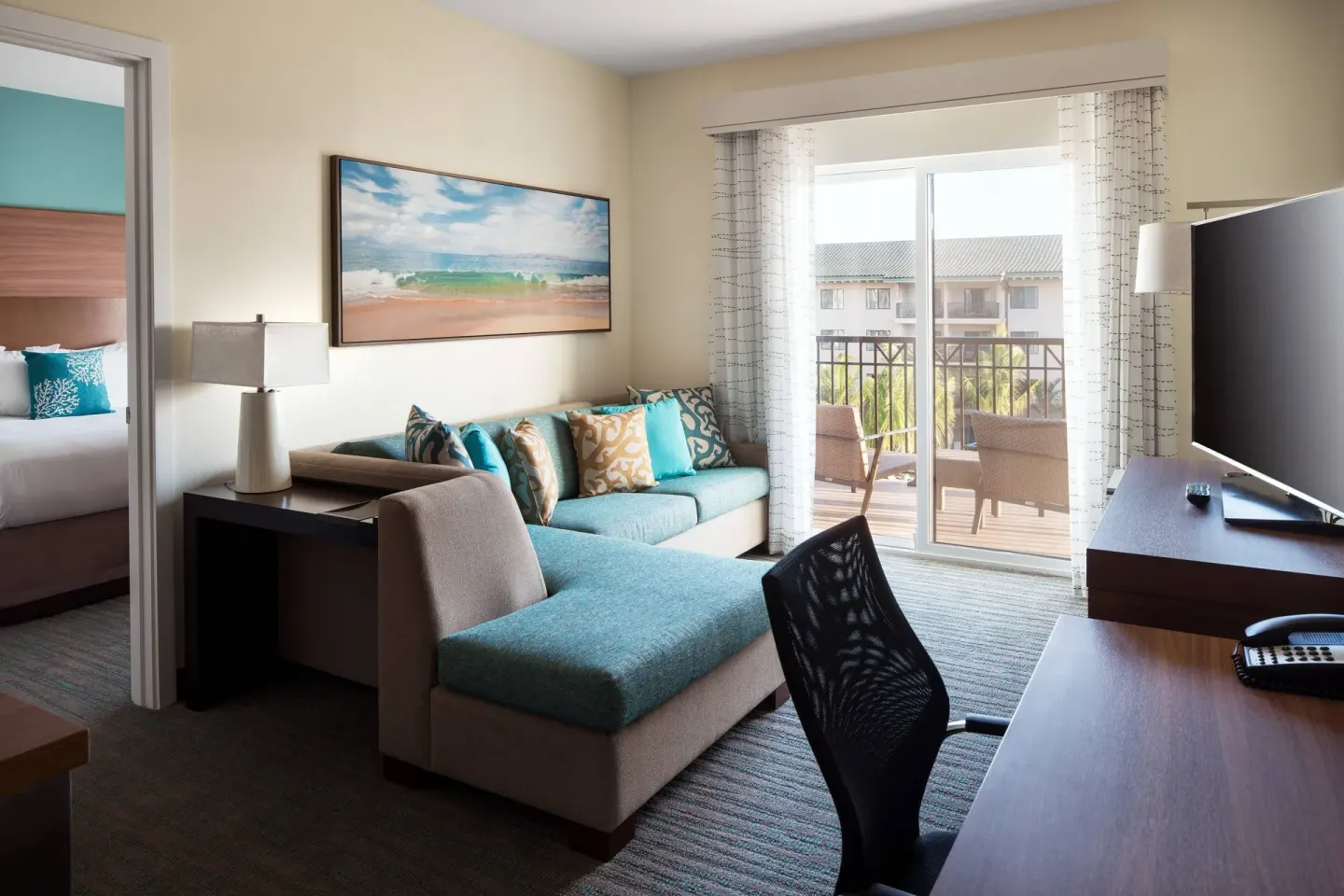Two-bedroom suite living area with sofa, desk, balcony, and bedroom at Residence Inn Maui Wailea.