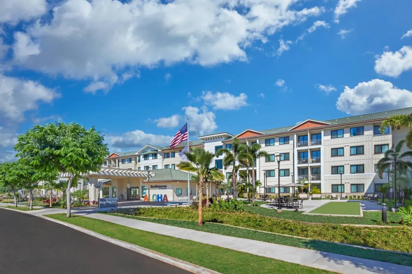 Wide daytime exterior with palms and entrance drive at Residence Inn Oahu Kapolei.