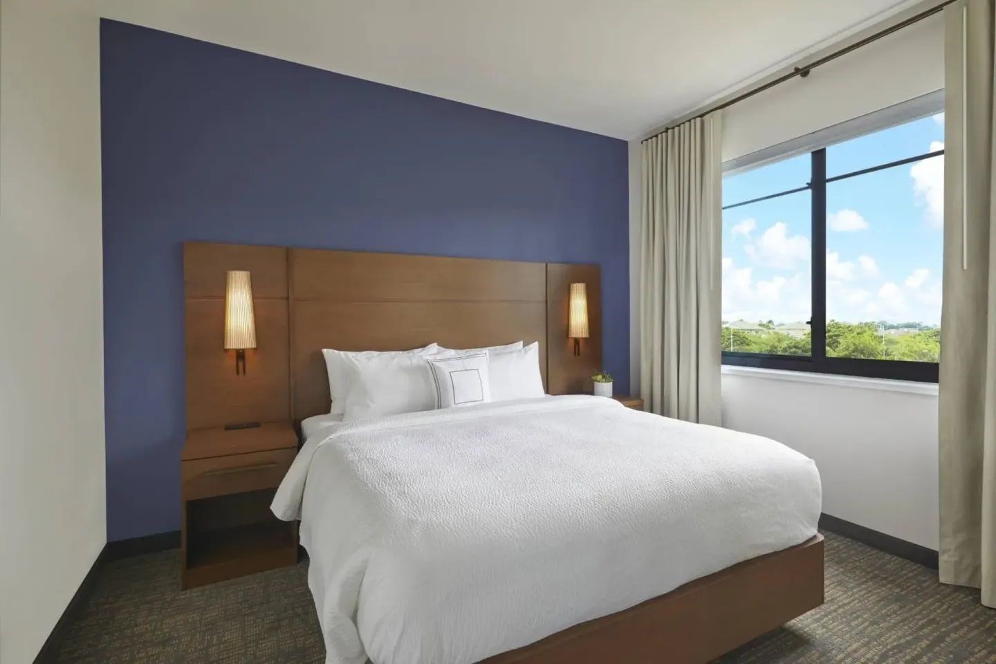 King bed guest room with blue accent wall and large window at Residence Inn Oahu Kapolei.