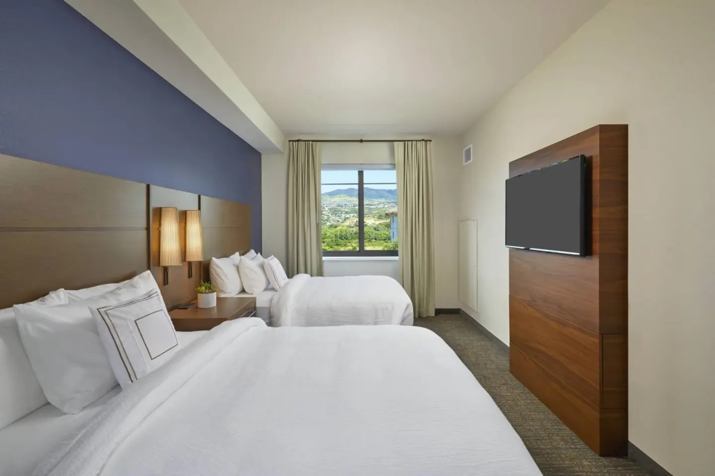 Guest bedroom with two beds, wall-mounted TV, and window view at Residence Inn Oahu Kapolei.