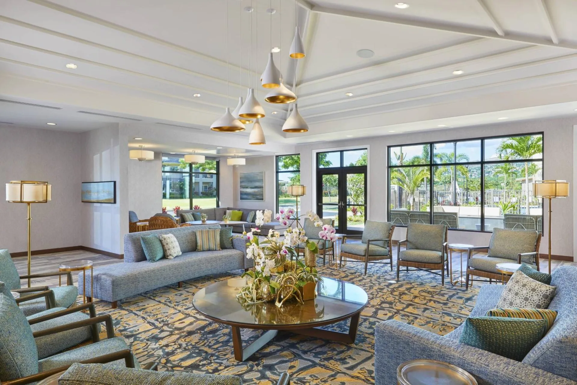 Lobby lounge with sofas, armchairs, pendant lights, and garden-facing windows at Residence Inn Oahu Kapolei.
