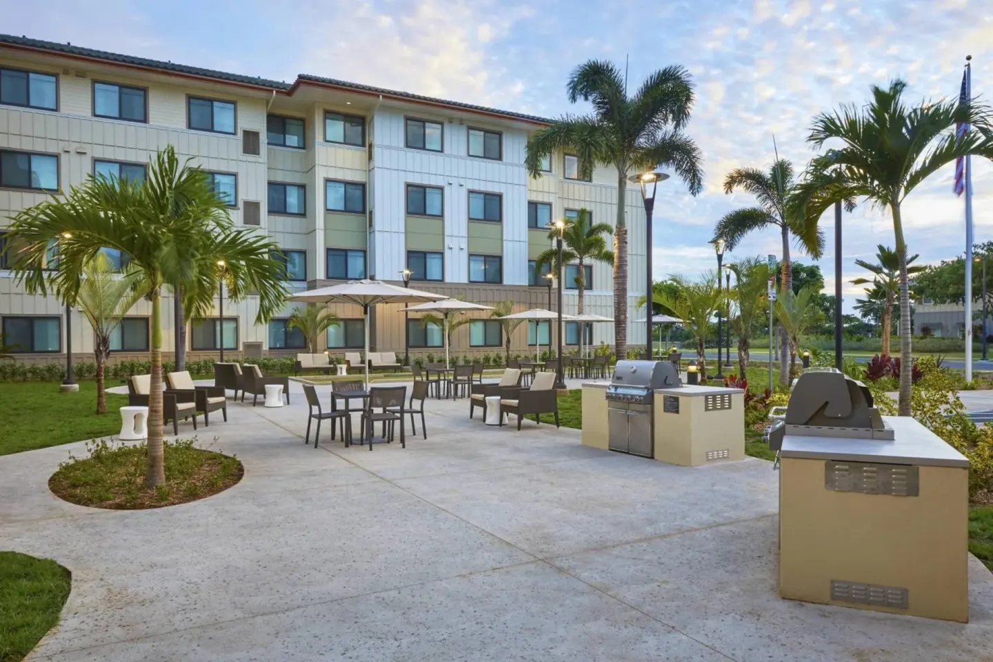 Outdoor patio with seating, grills, umbrellas, and palms at Residence Inn Oahu Kapolei.