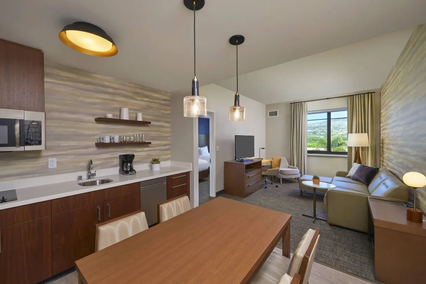 One-bedroom suite living area with kitchen, dining table, sofa and bedroom doorway at Residence Inn Oahu Kapolei.