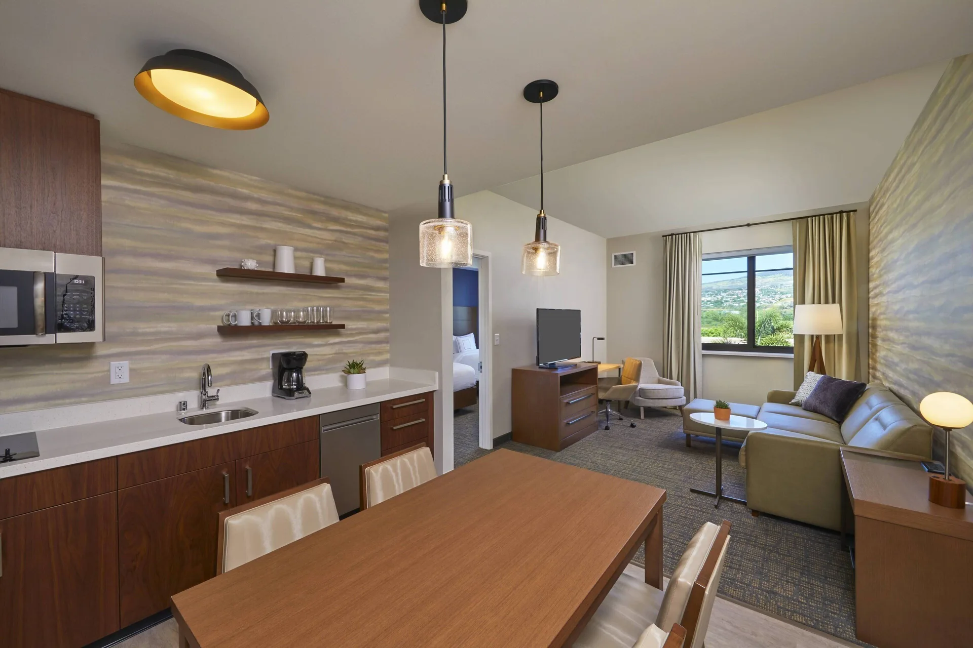One-bedroom suite living area with kitchen, dining table, sofa and bedroom doorway at Residence Inn Oahu Kapolei.