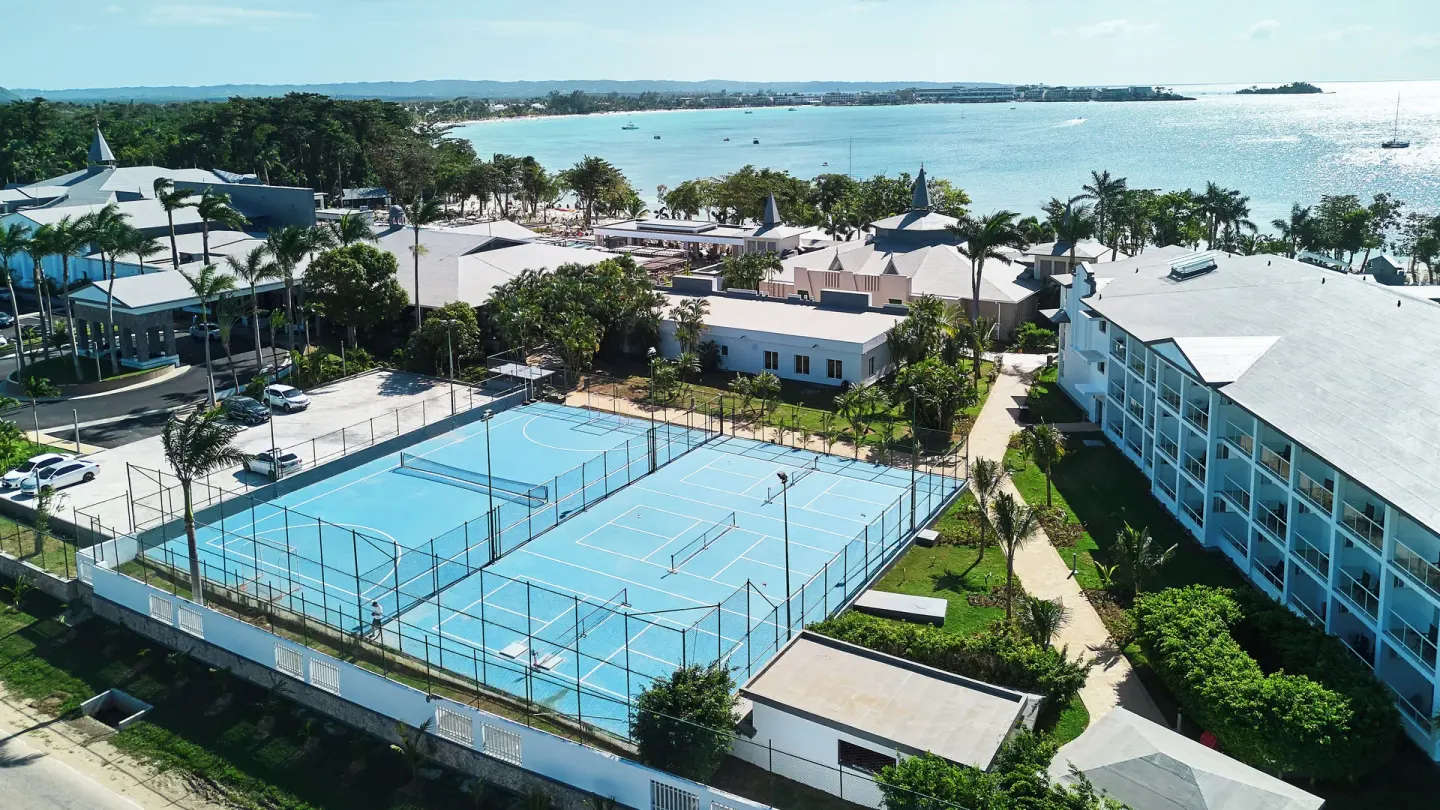 Aerial view of blue sports courts, resort buildings, and the bay at Riu Negril.