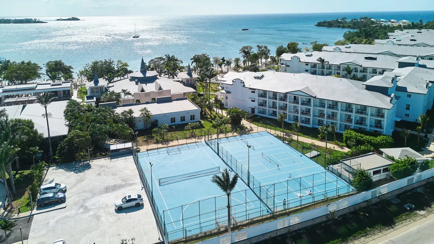 Aerial view of sports courts, resort buildings, palms, and shoreline at Riu Negril.