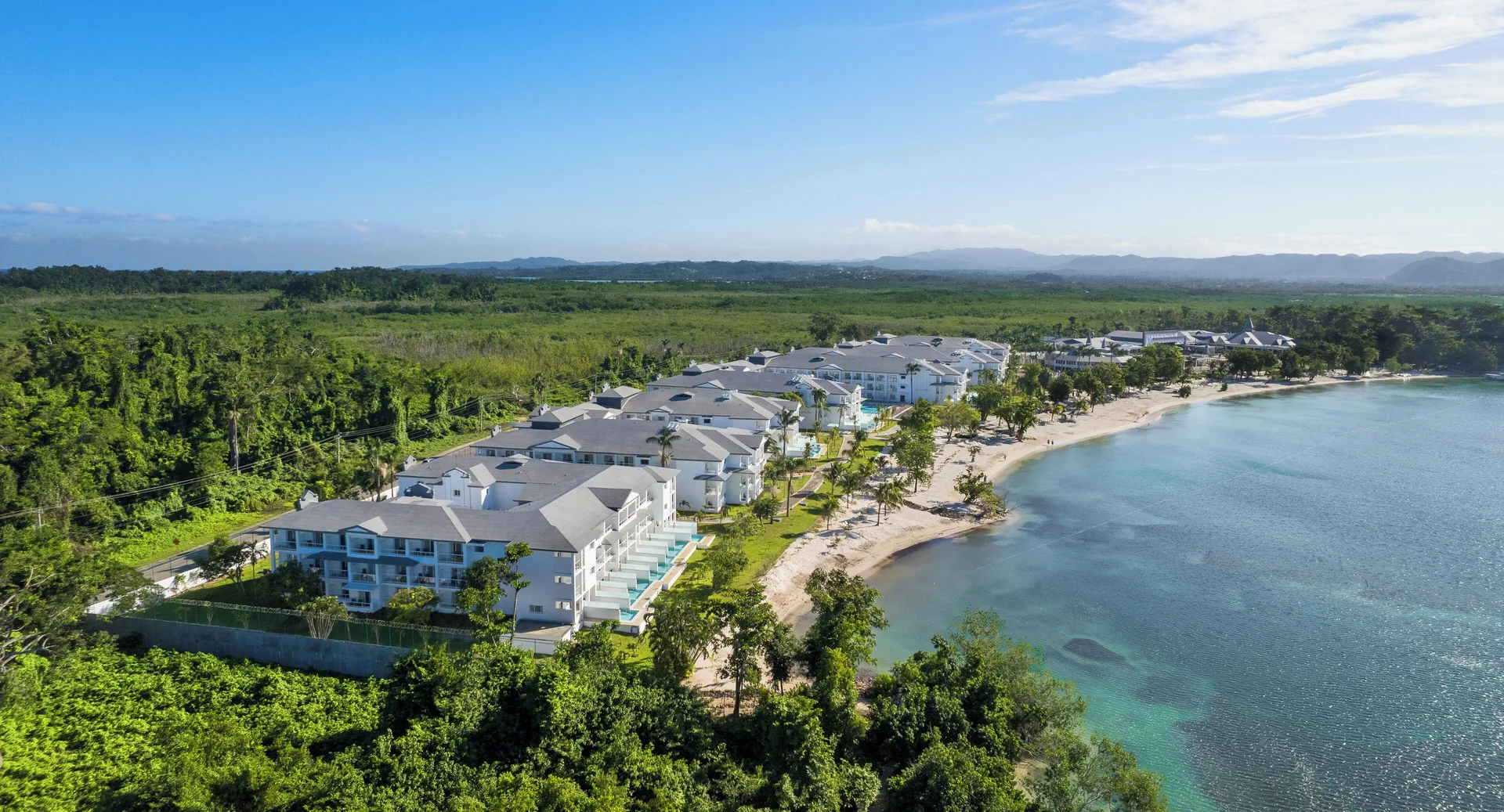 Aerial view of Riu Negril resort buildings along a calm bay and sandy beach.