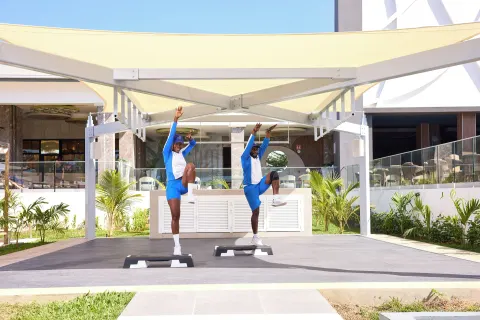 Two instructors stretch on step platforms under a canopy at Riu Negril.