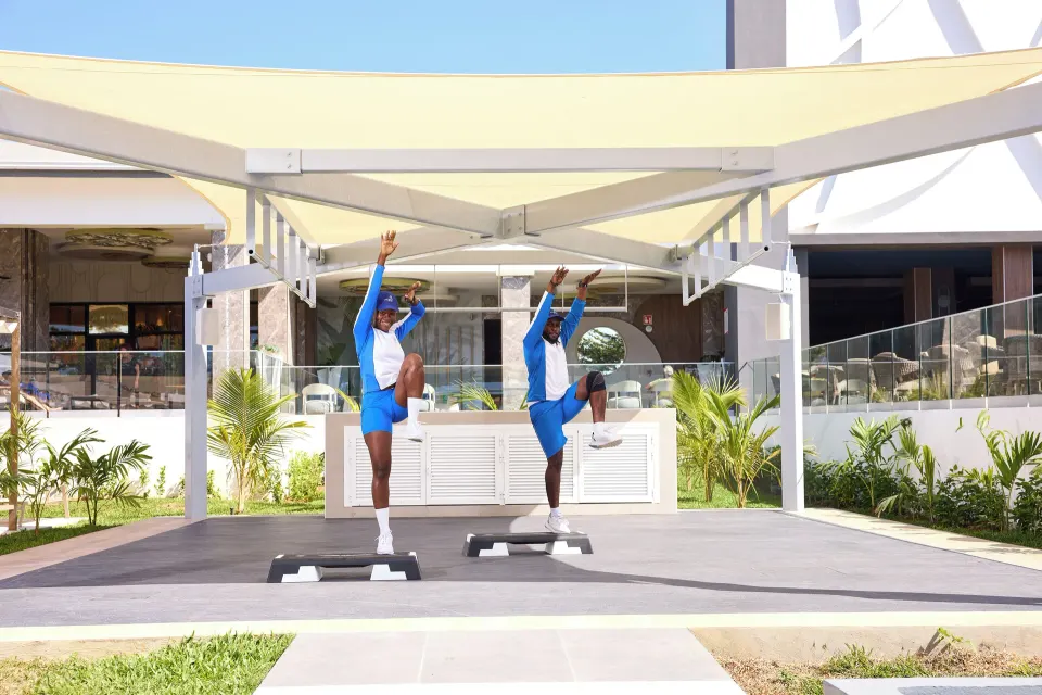 Two instructors stretch on step platforms under a canopy at Riu Negril.