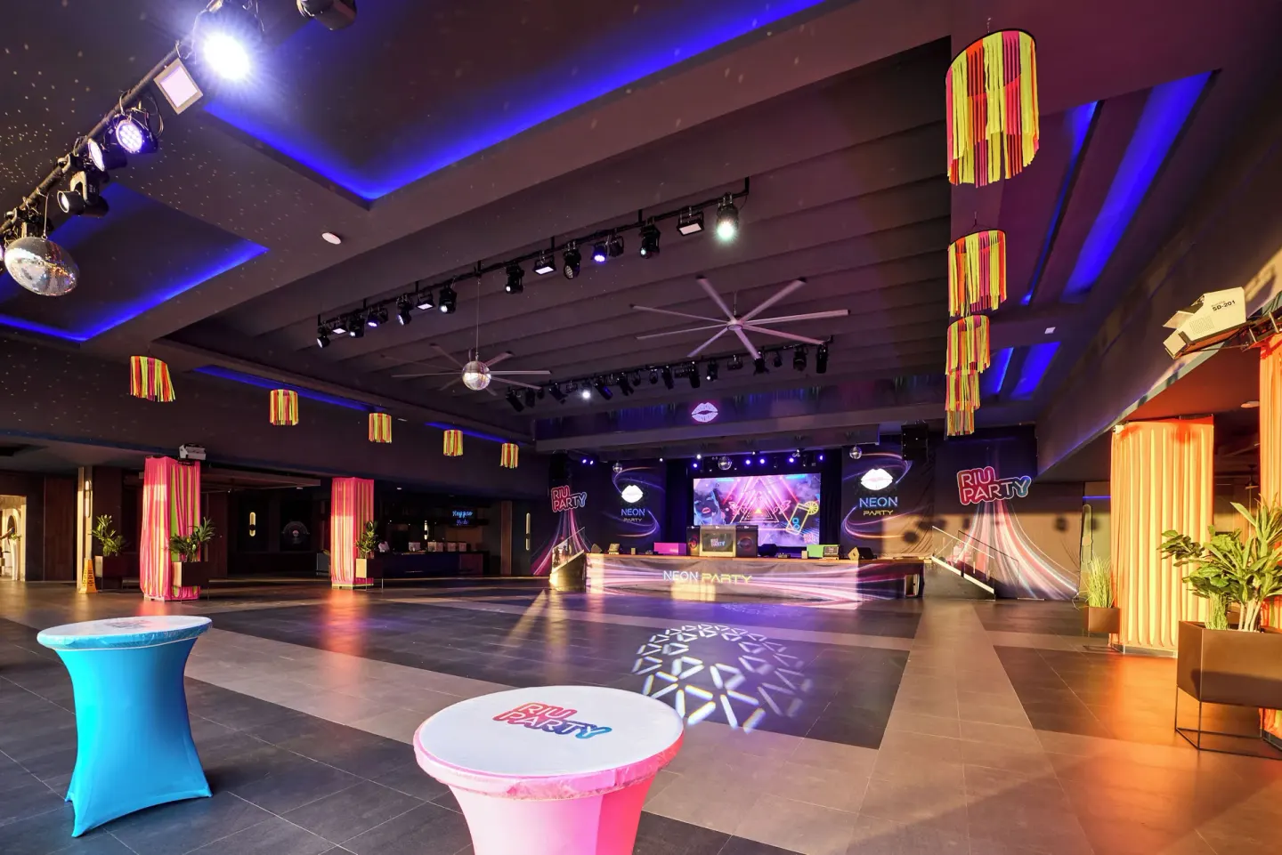 Indoor neon party venue with stage lighting and cocktail tables at Riu Negril.