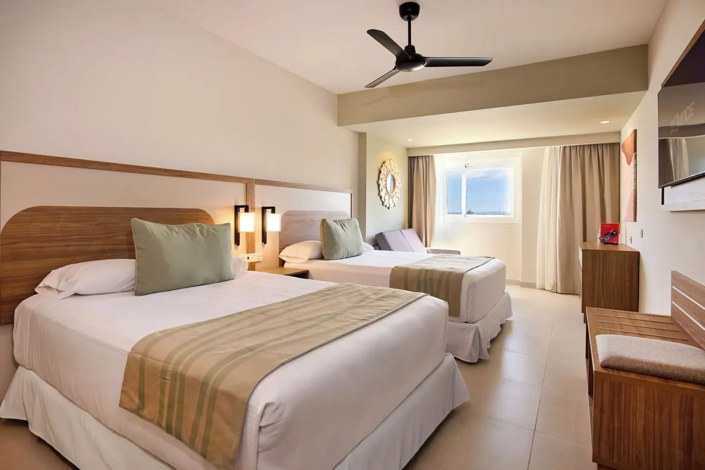 Family Room at Riu Negril with two beds, seating, TV, ceiling fan, and window.