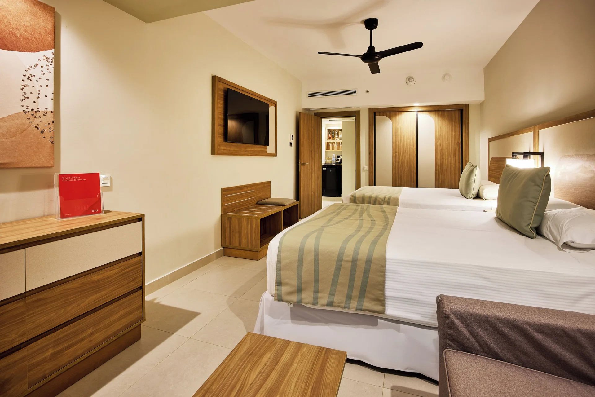 Family Room at Riu Negril with two beds, wall TV, dresser, bench, and wardrobe.