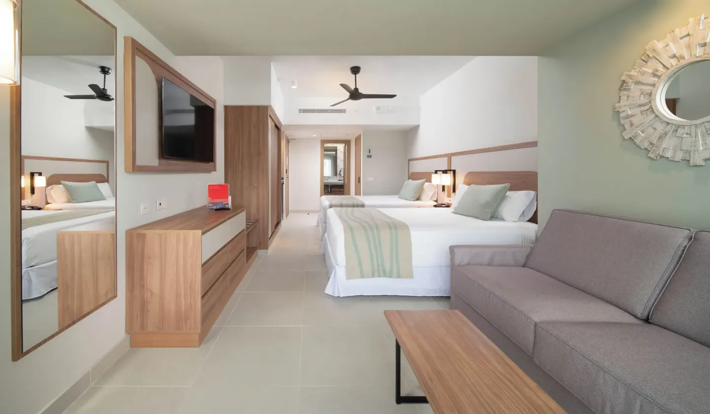 Oceanfront guest room with two beds, sofa, TV, and wood furnishings at Riu Negril.