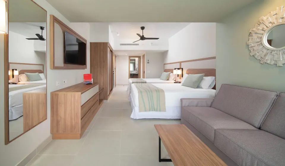 Oceanfront guest room with two beds, sofa, TV, and wood furnishings at Riu Negril.
