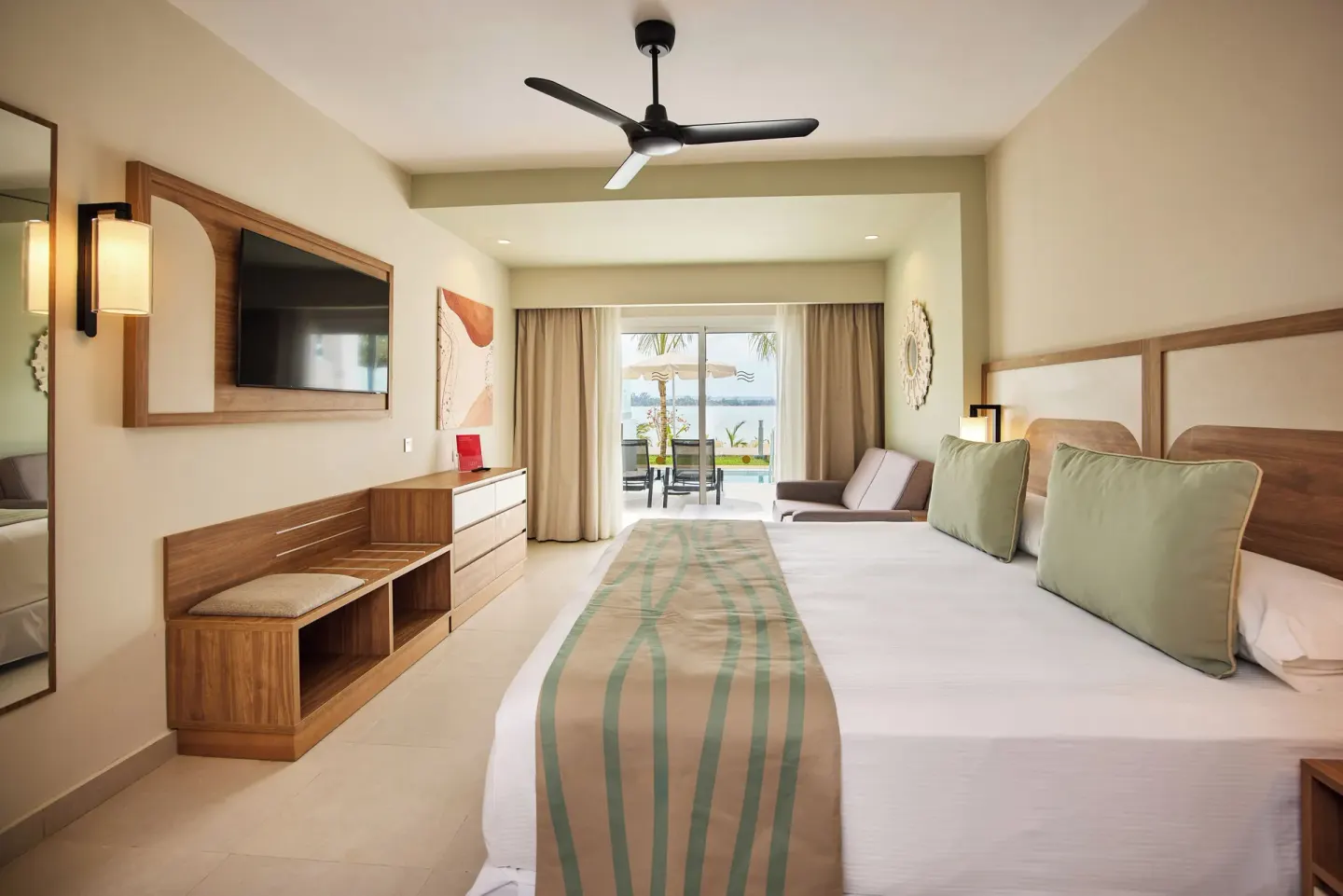 King bed guest room with TV wall and patio view at Riu Negril.