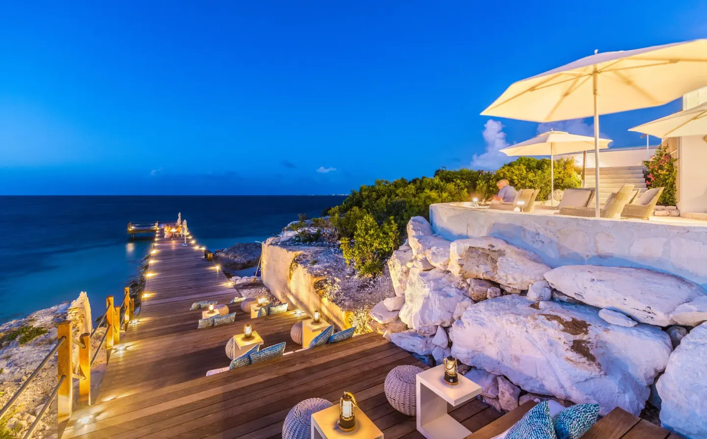 Cliffside decks with lounge seating, umbrellas, and a lit pier at Rock House.
