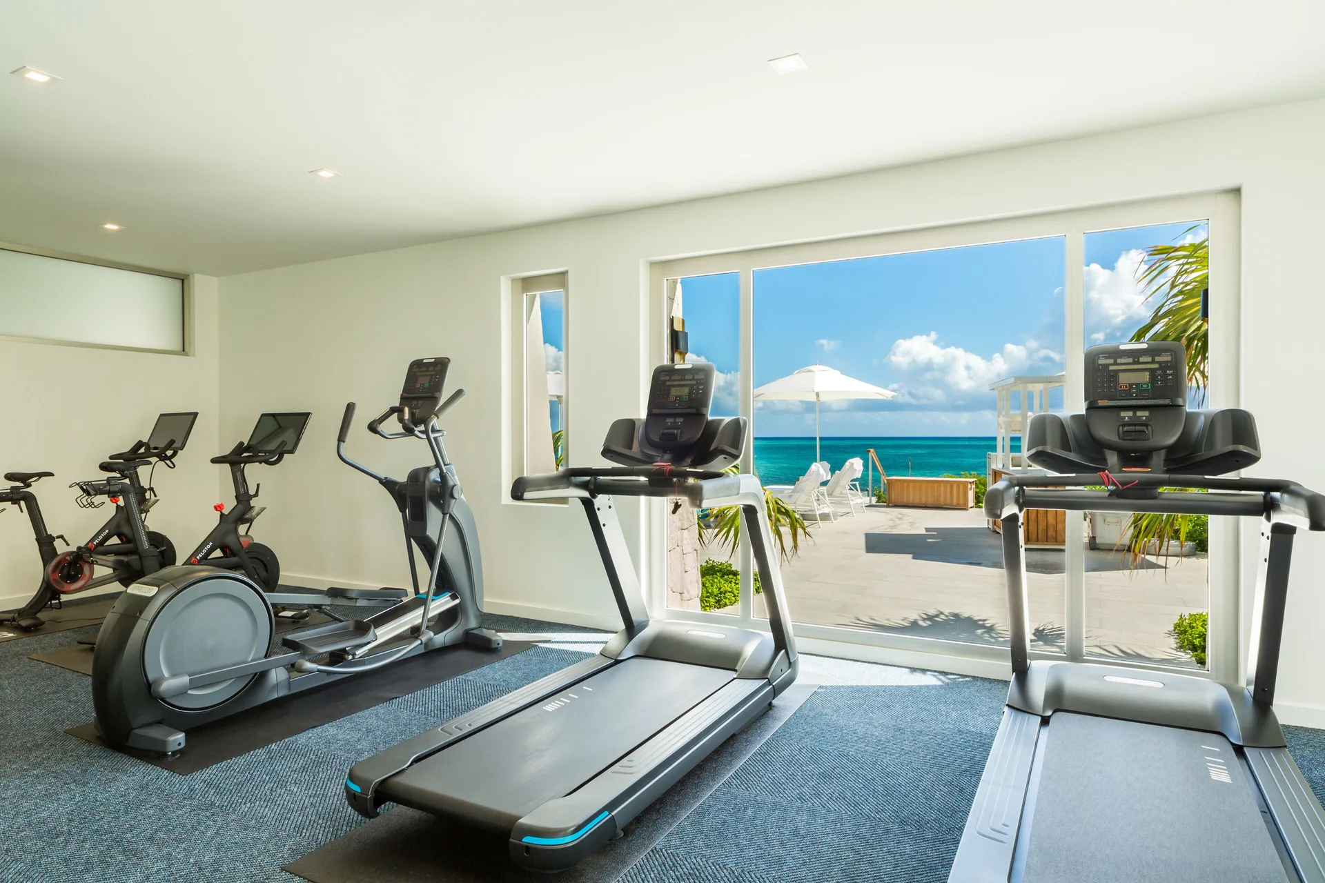 Fitness room at Rock House with treadmills, bikes, an elliptical, and ocean-facing windows.
