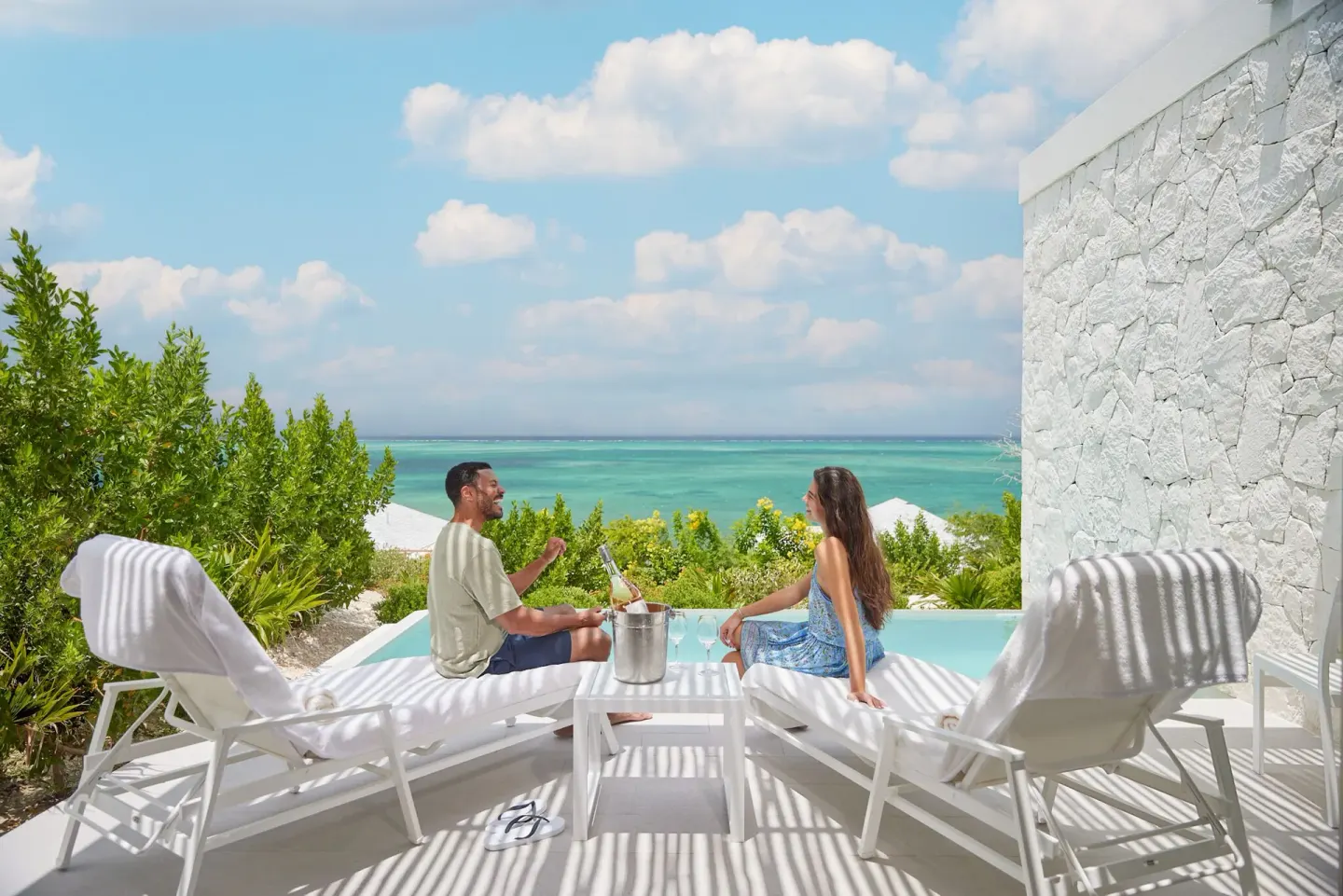 Couple relaxing on white loungers by a plunge pool with ocean view at Rock House.